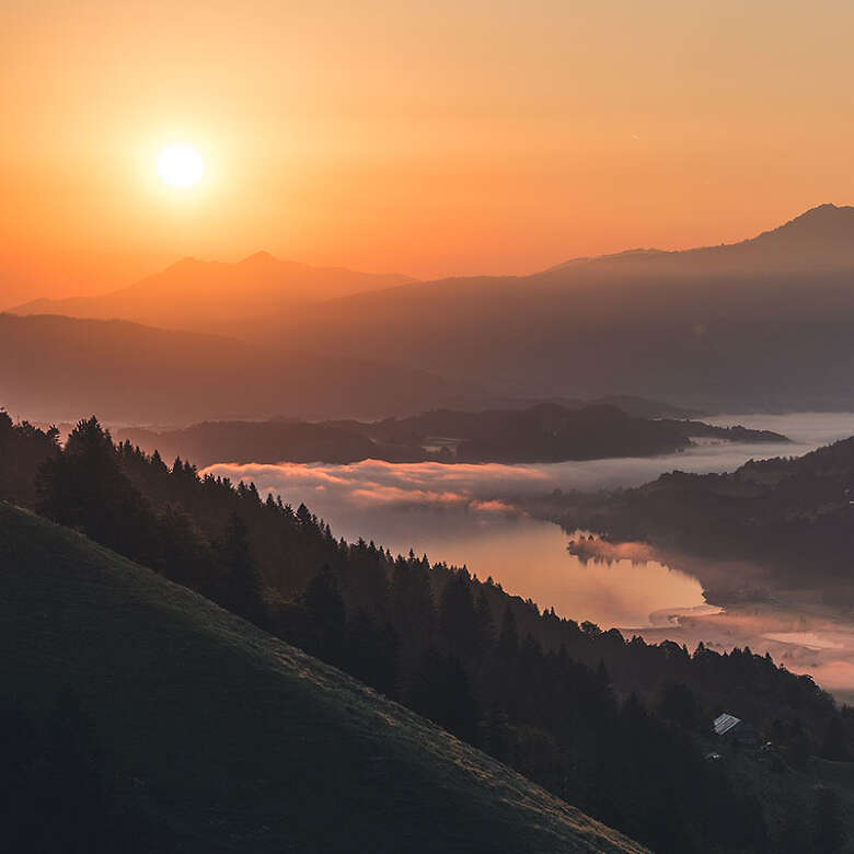 Sonnenaufgang über dem Großen Alpsee im Nebel mit Bergpanorama