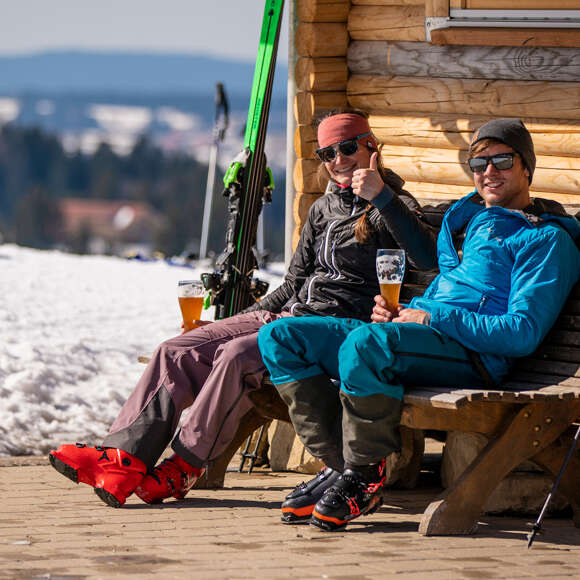 Paar sitzt an einer Holzhütte beim Einkehren am Skitag.
