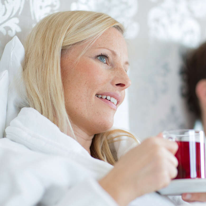 Frau hält eine Teetasse in der Hand und blickt verträumt in die Ferne.