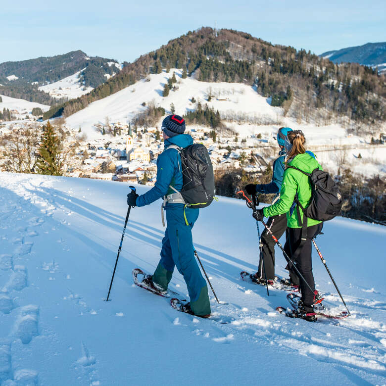Drei Schneeschuhwanderer an einem sonnigen Wintertag über Oberstaufen.