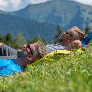 Zwei Männer liegen mit den Köpfen auf ihren Rucksäcken im Gras. Im Hintergrund der Hochgrat.
