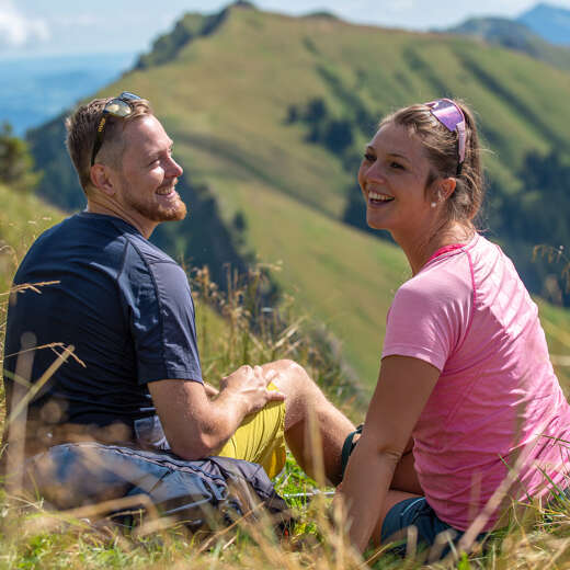 Ein Mann und eine Frau sitzen im Gras. Im Hintergrund der Bergrücken des Rindalphorns.