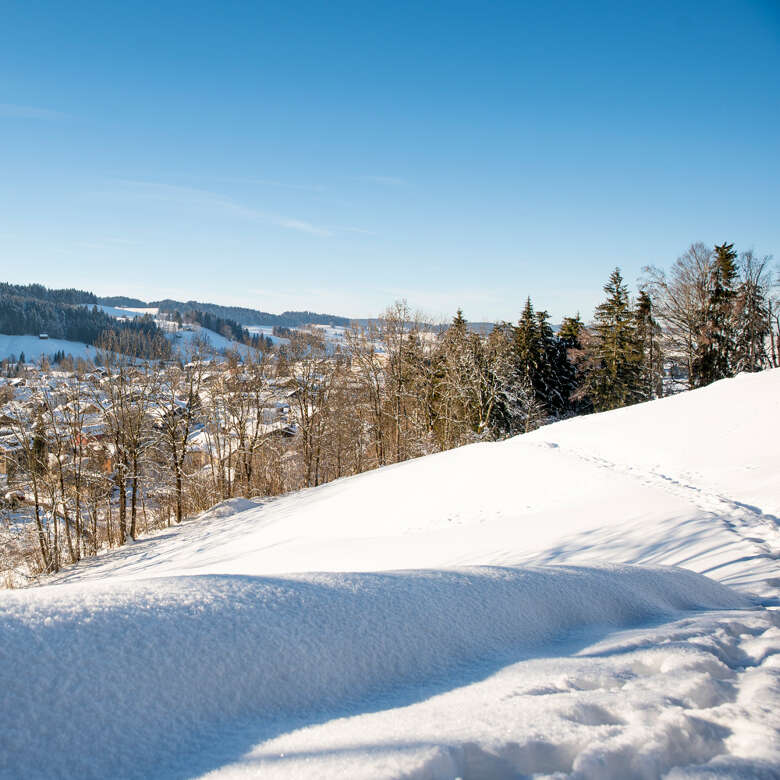 Verschneite Winterwanderweg mit Ortsblick bei Oberstaufen.