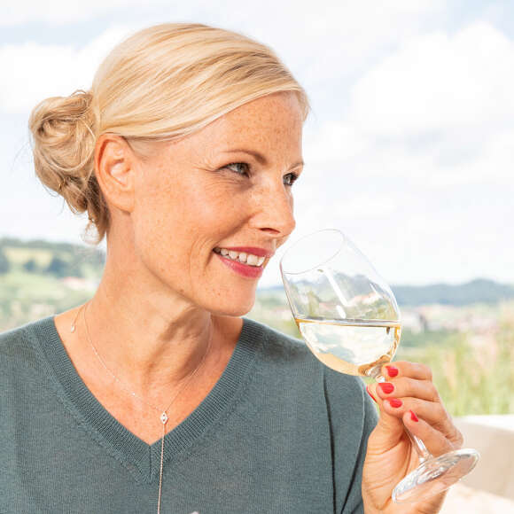 Blonde Frau riecht an einem Glas Weißwein.