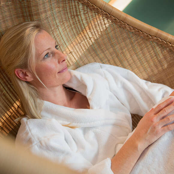 Frau entspannt im Bademantel in einem Hängesessel aus Rattan.