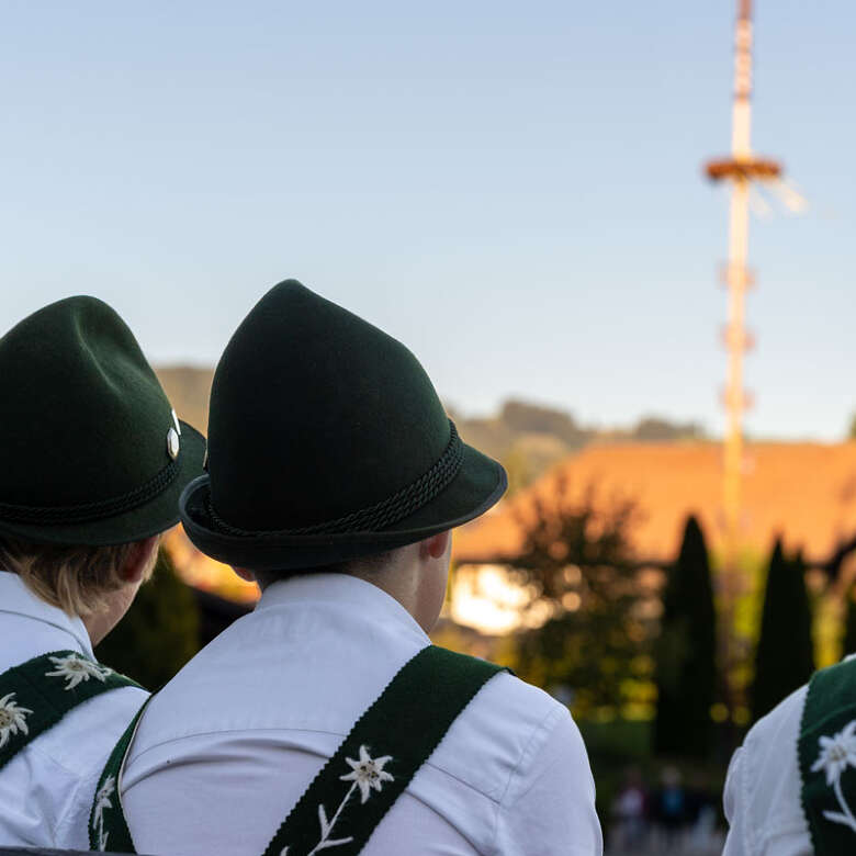 Volkstanz Bubn Tracht Huimatwochen 2026 Volkstanz Bubn sitzen in Tracht auf Bank mit Blick Maibaum bei den Huimatwochen