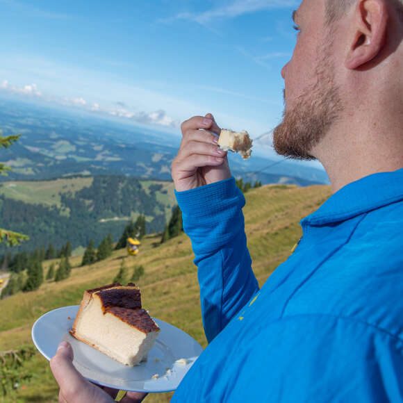 Mann isst einen Kuchen auf dem Staufner Haus mit Ausblick über Oberstaufen.