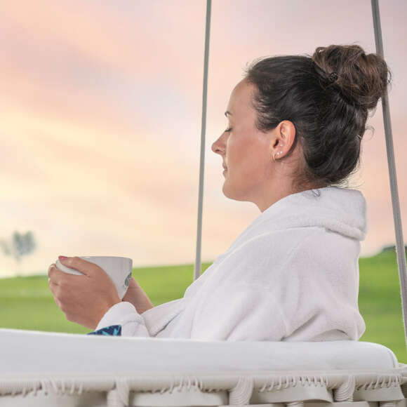 Wellnessen in Oberstaufen Eine Frau sitzt in einer Schaukel bei Sonnenuntergang.