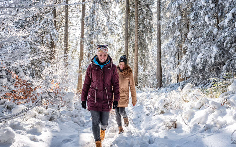 Winterwandern in Oberstaufen Zwei Freundinnen wandern durch den Winterwald bei Oberstaufen